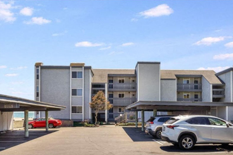 A parking lot in front of a multi-story apartment building with cars parked.